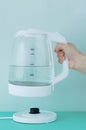 White glass teapot with water in hand. Puts the kettle on electric platform