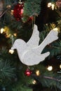 White glitter dove and red bell ornament hanging on Christmas tree