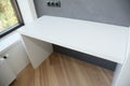 A white gloss computer table on the wood laminate floor near the window with radiator and painted gray wall with black European