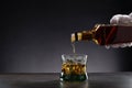 White gloved hand pouring whisky into a glass with ice on dark background, with copy space Royalty Free Stock Photo