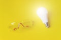 White glowing light bulb and Builder`s safety glasses Against Yellow Background. Idea, innovation, creativity concept, design Royalty Free Stock Photo