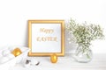 White and gold Easter eggs, a mockup with a gold frame and spring flowers in a vase on a white wooden table Royalty Free Stock Photo