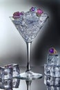 White gold jewelry with amethysts and blue topaz in a martini glass with ice and ice cubes on a gray background with reflection. Royalty Free Stock Photo