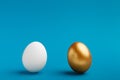 White and golden eggs on blue background, copy space