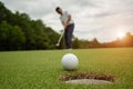 White golf ball rolling down golf hole on putting green with evening golf course Royalty Free Stock Photo