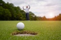 White golf ball rolling down golf hole on putting green with evening golf course backdrop Royalty Free Stock Photo