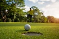 White golf ball rolling down golf hole on putting green with evening golf course backdrop Royalty Free Stock Photo