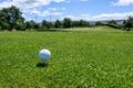 White golf ball sitting on a white tee in the tee box, hole long way in the distance Royalty Free Stock Photo