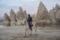 White gorgeous horse with male tourist on his back at strange formations sandstone in Love Valley