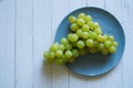 Healthy eating. White grapes lie in a blue plate on a light natu