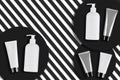 White, gray tubes and pump bottles with no logo or label on black round stands, striped background. Cosmetics packs