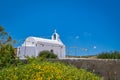 White Greek Orthodox chapel or church on top of hill against clear blue sky on sunny day. Colorful flowers and bushes in Royalty Free Stock Photo