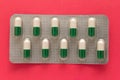 White and green capsules in medicine box. Pills over red background. Royalty Free Stock Photo