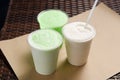White and green milkshakes in transparent cups with a straw