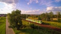 White and green train passing through small village during sunny evening.