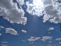 White and grey fluffy rain clouds glowing in front of the sunrays in the blue sky