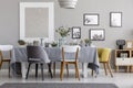 White, grey and yellow chair at table in dining room interior with posters. Real photo