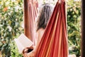 White hair diversity senior woman relax on an hammock in the garden at home reading a paper book and enjoying the quaity of