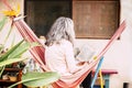 White hair diversity senior woman relax on an hammock in the garden at home reading a paper book and enjoying the quaity of