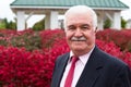 White Hair Senior Businessman Outside by the Red Burning Bushes