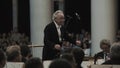 White-haired kapellmeister conducting string orchestra in classic concert hall