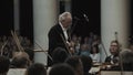 White-haired kapellmeister conducting string orchestra in classic music hall