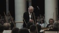 White-haired kapellmeister conducting violin orchestra in classic concert hall