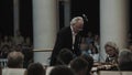 White-haired kapellmeister directing string orchestra in classic music hall