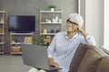 Portrait of happy mature woman sitting on sofa at home, holding laptop and smiling Royalty Free Stock Photo