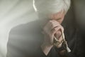 Of white haired senior priest praying with rosary in serene god rays