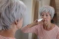 A white haired senior woman in her sixties is using a nasal spray in front of the bathroom mirror Royalty Free Stock Photo