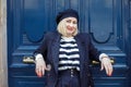 White-haired woman with beret smile leaning against door outdoor. Lady with blue eyes, red lips wear stylish clothes.