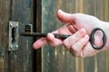 white hand putting an old or vintage key made by metallic iron inside a lock of a wooden door. The old key and the lock are Royalty Free Stock Photo