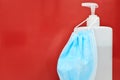 White hand sanitizer or soap dispenser and a blue face mask in red background with copy space Royalty Free Stock Photo