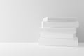 White hardcover books with blank covers stacked on white table or shelf against white wall background