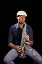 With white hat a black man is sitting and playing his saxophone, dark background, nice music Royalty Free Stock Photo