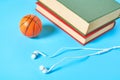 White headphone and old books, toy basketball ball on blue background Royalty Free Stock Photo