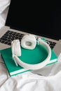 White headphones, green book and laptop in a white bed.