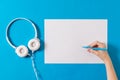 White headphones, a piece of paper and a hand with a marker on a blue background. Royalty Free Stock Photo