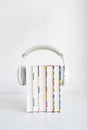 white headphones on a stack of 5 books on a table against a white wall background. audiobook concept.