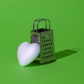 White heart and small grater on a green background. Harsh shadow. Love, life, brokenhearted, message, culinary arts, concept.