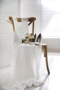 White high heel shoes, flowers and wedding dress on wooden chair indoors Royalty Free Stock Photo