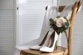 White high heel shoes  flowers and wedding dress on wooden chair indoors. Space for text Royalty Free Stock Photo