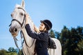 Appealing horsewoman smiling while looking at her gentle white horse