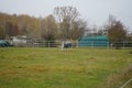 A white horse under a gray papon grazes in a paddock pasture at the Stadtrandhof, Waltersdorfer Chaussee, 12529 Schoenefeld