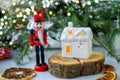 White house in the form of a ceramic candlestick on the background of decorative branches with a Nutcracker figure-Christmas card