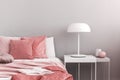 White industrial lamp on simple nightstand table next to cozy bed with pink bedding