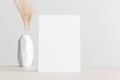 White invitation card mockup with a dried grass on a beige table. 5x7 ratio, similar to A6, A5