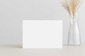 White invitation card mockup with a dried grass on a beige table. 5x7 ratio, similar to A6, A5