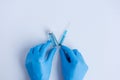 On white isolated background, hands of doctor in medical blue gloves hold an ampoule with syringe
